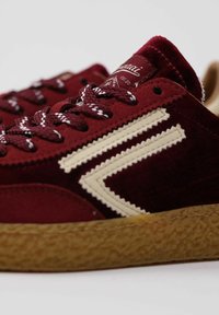 Sneaker bordeaux con una parte superiore in velluto testurizzato, accenti crema, design distintivo a zigzag e suola in gomma nocciola. Presenta lacci bianchi e bordeaux.