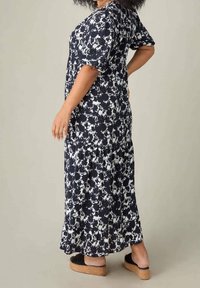 Maxiklänning i marinblå och vit blommönster, korta ärmar, mjukt tyg, med en plisséklänning och platta svarta sandaler med korksulor.