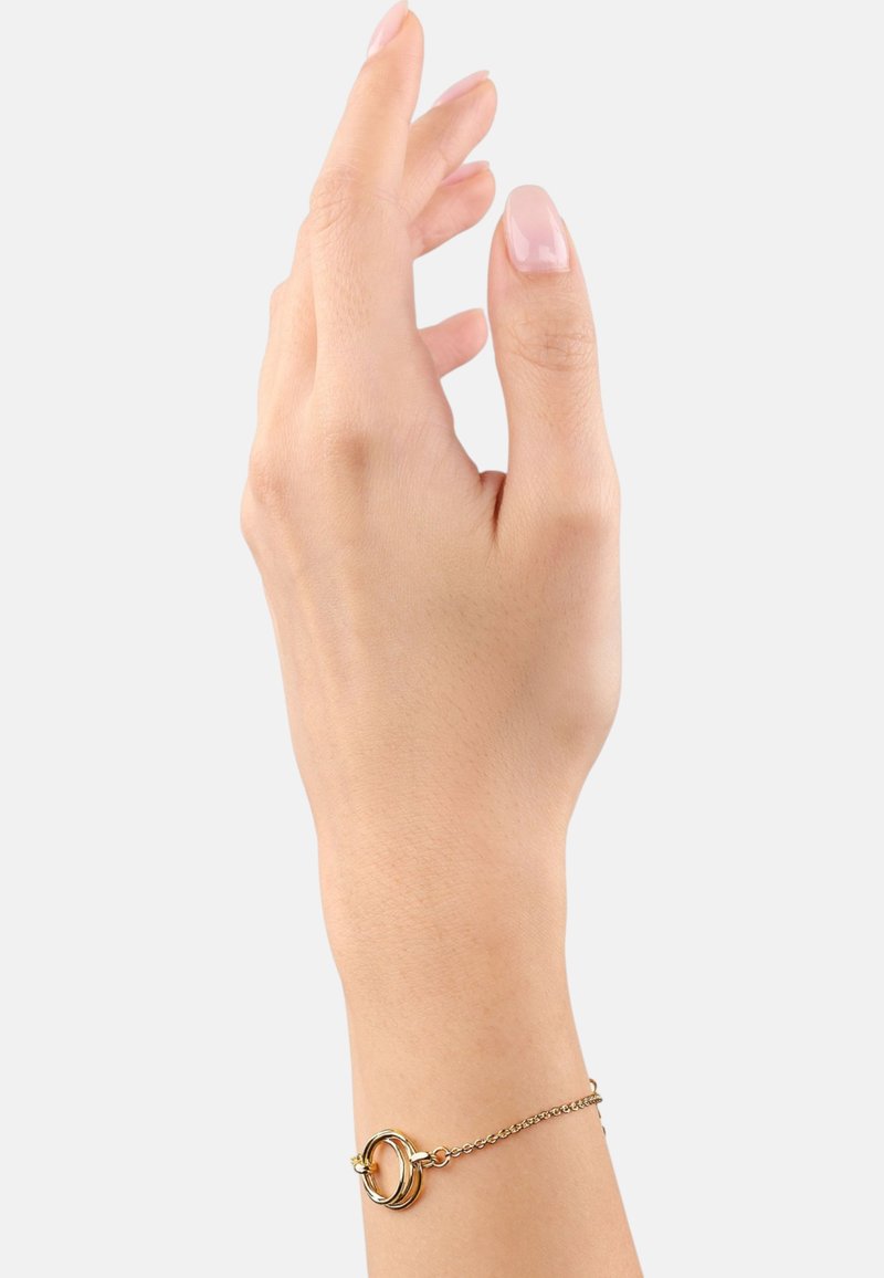 Goldarmband mit einer dünnen Kette und zwei ineinandergreifenden Ringen. Hat eine glatte Textur und ein minimalistisches Design. Wird an einer Hand mit hellen Hautton getragen.