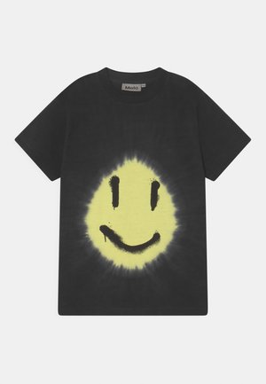 Sort T-shirt med korte ærmer med et stort gult smilende ansigt med sorte øjne og mund med en spraymalingseffekt i midten.