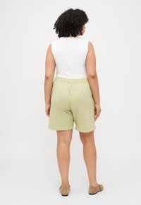 Top blanco sin mangas combinado con pantalones cortos ligeros verdes de longitud a la rodilla, con un ajuste relajado y cinturilla elástica.