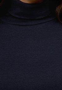 Donkerblauwe turtleneck trui gemaakt van ribbenstructuur stof, met een strakke pasvorm rond de hals en het lichaam, zonder zichtbare patronen of versieringen.