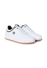 Para białych sneakersów niskich z czarnymi wykończeniami, białymi sznurówkami, gumowymi podeszwami oraz czarnym logo "C" po zewnętrznych stronach i na języku.