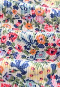 Tessuto di cotone floreale con una texture a righe, decorato con un motivo colorato di fiori rossi, blu e gialli su uno sfondo crema.