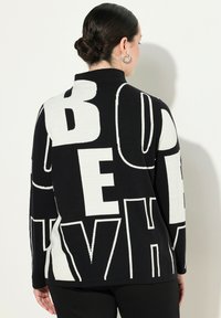 Maglione lavorato a maglia bianco e nero con grande testo grafico sul retro. Texture morbida, maniche lunghe e design con colletto alto.