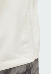 T-shirt beige clair en tissu doux, avec un ourlet plat et le texte "climacool" en blanc sur le côté. Coutures visibles.