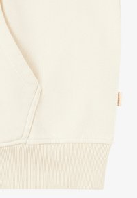 Helle Hoodie-Details mit einer Kängurutasche, gerippten Bündchen und einem kleinen Etikett an der Seite. weicher, strukturierter Stoff.