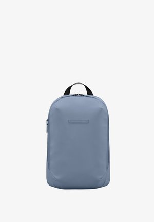 Sac à dos bleu clair fabriqué en matériau lisse, avec un design arrondi, une poignée supérieure et un accent avant minimaliste.
