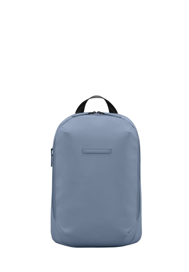 Sac à dos bleu clair fabriqué en matériau lisse, avec un design arrondi, une poignée supérieure et un accent avant minimaliste.