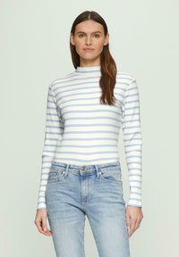 Langärmliges, geripptes Oberteil in hellblau und weißen Streifen mit hohem Kragen. Kombiniert mit hellblauen Jeans.