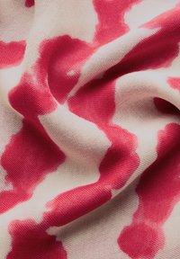 Tejido de algodón con una base color crema y manchas irregulares en rosa, que muestra una textura suave y ligera, así como un caído fluido.