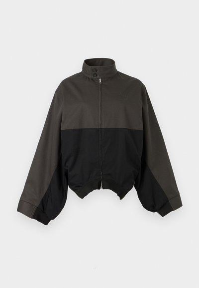 Μαύρο και σκούρο γκρι μπουφάν με φερμουάρ και ψηλό γιακά, με κουμπωτή ταινία και μανίκια σε στυλ μπαλόνι, εμφανίζεται πάνω σε λευκό φόντο.