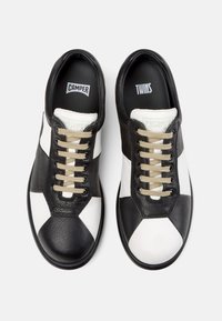 Mustat ja valkoiset nahkakengät, joissa on rakenne pinta, esitetty kuusikulmainen kuvio, pyöreät beige nauhat ja mustat kumipohjat.