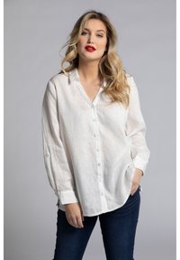 Camisa de lino blanca de botones, con mangas largas, corte relajado y aberturas laterales. Presenta un cuello clásico y botones de color azul claro.