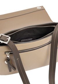 Beżowa skórzana torebka na ramię z zamkiem błyskawicznym, szarym paskiem na ramię i srebrnymi okuciami. Wnętrze wyściełane czarną podszewką.