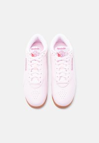 Ζευγάρι ανοιχτόροζ αθλητικά παπούτσια Reebok με λευκά κορδόνια, κόκκινο λογότυπο στη γλώσσα και στο πλάι, και καφέ λαστιχένιες σόλες σε λευκό φόντο.