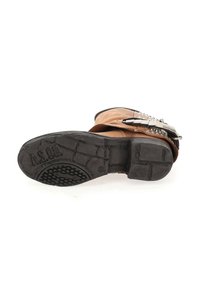 Bottine en cuir marron avec semelle en caoutchouc noir, accents en métal argenté et détails cloutés sur le côté. Surface texturée et forme épaisse.