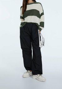Green and white striped knit sweater, black loose-fit trousers, and chunky white platform shoes, complemented by a small crossbody bag.