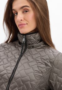 Grau gesteppte Jacke mit Stehkragen, Frontreißverschluss und strukturiertem Rautenmuster. Hat kontrastierende schwarze Besätze und einen eleganten Reißverschluss-Zug.