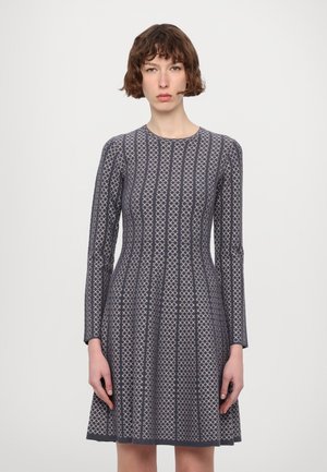 Abito a maglia a maniche lunghe di colore grigio scuro con motivo geometrico. Presenta un collo rotondo e una gonna svasata che arriva sopra il ginocchio.