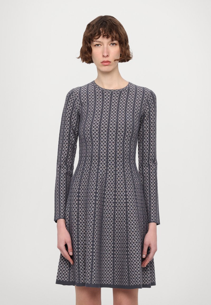 Abito a maglia a maniche lunghe di colore grigio scuro con motivo geometrico. Presenta un collo rotondo e una gonna svasata che arriva sopra il ginocchio.