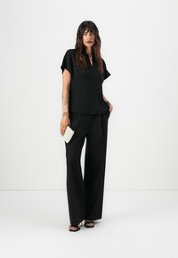 Top corto nero con scollatura a V e maniche corte abbinato a pantaloni neri larghi. Tiene una pochette bianca testurizzata. Sandali neri semplici.