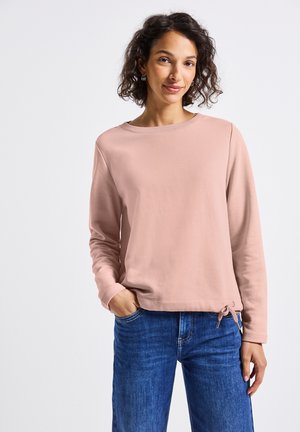 Sweatshirt rose clair avec un col rond, des manches longues et un bas à cordon de serrage. Associé à un jean en denim bleu. Texture lisse.
