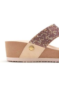 Sandale compensée beige en matériau doux et texturé, avec une sangle en accent pailleté violet et un détail de logo en métal rond. Semelle plate avec adhérence.