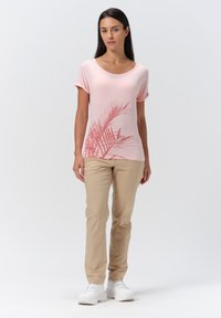 Camiseta de manga corta rosa claro con estampado de hojas de palma, combinada con pantalones beige y zapatillas blancas. Textura suave, ajuste relajado.