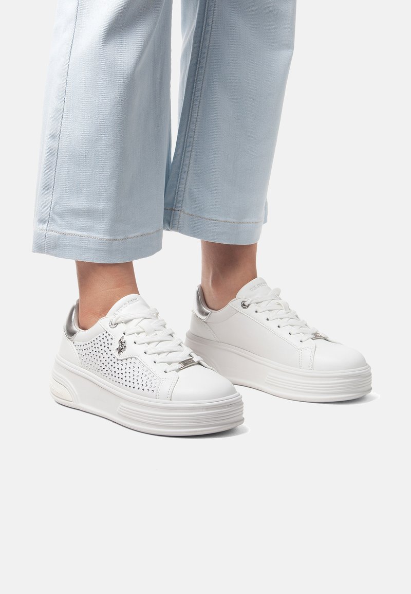 Vita sneakers med perforerat mönster, silverdetaljer, rund tå och tjocka vita sulor. Bärs med ljusblå vida jeans.