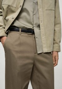 Giacca corduroy beige, camicia verde chiaro, cintura nera e pantaloni marroni. Concentrarsi sulla texture, sulla coordinazione dei colori e sui dettagli della vestibilità su misura.