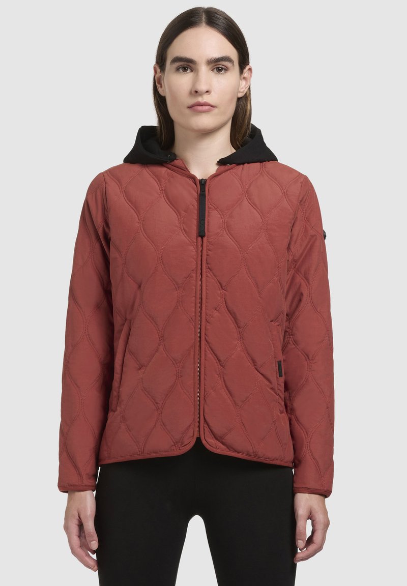Giacca trapuntata rossa con cappuccio nero, dotata di una cerniera frontale, motivo a diamante e una texture liscia, progettata per calore e comfort.