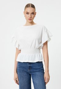 Hvid tekstureret bluse med korte rynkede ærmer og elastisk talje, parret med blå denimbukser. Enkel og elegant design.