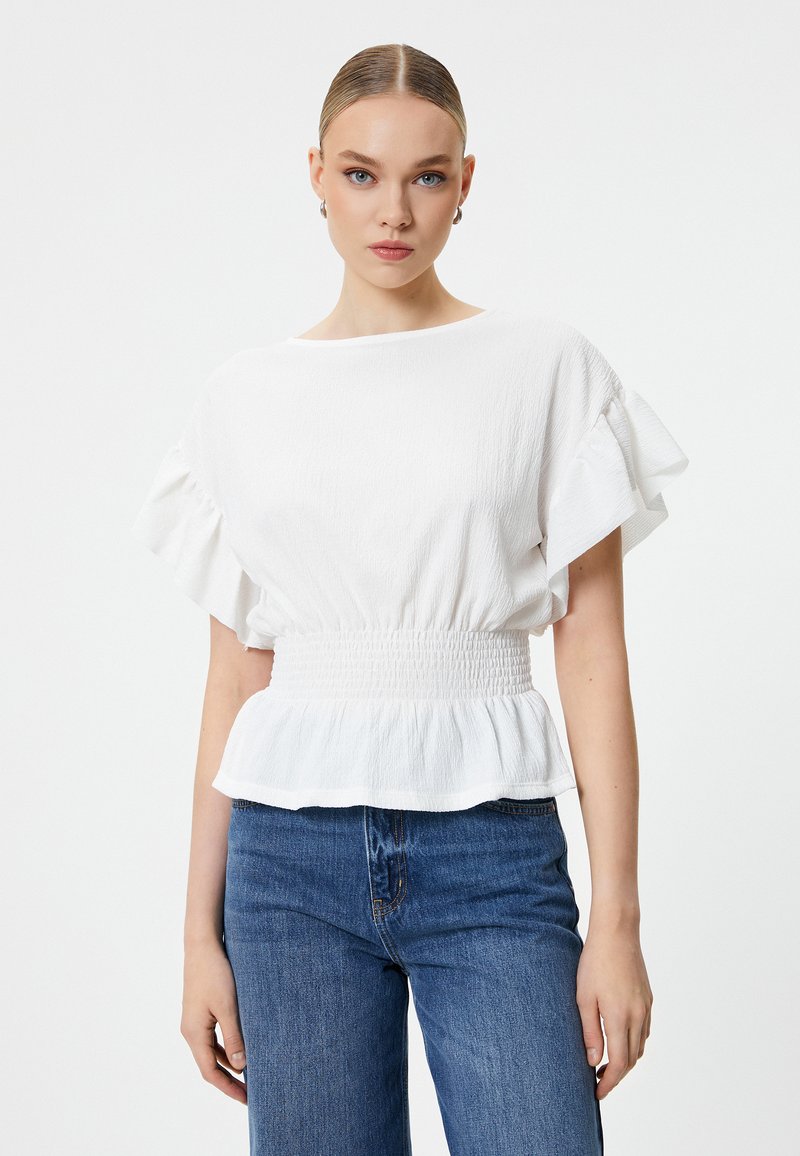 Hvid tekstureret bluse med korte rynkede ærmer og elastisk talje, parret med blå denimbukser. Enkel og elegant design.