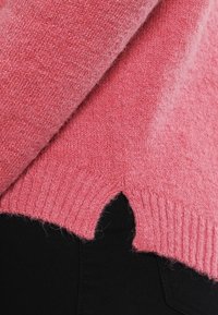 Pink knitted sweater with a soft texture, featuring a ribbed hem and a unique cut-out design at the bottom.