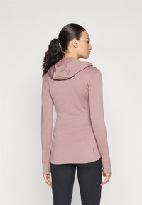 Moletom de manga longa rosa claro com capuz ajustável, mangas longas e bainha curvada, feito de um tecido suave e texturizado.