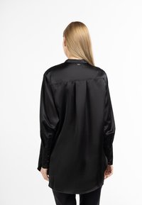 Sort satin langærmet skjorte med knappede manchetter, en rygfold, en spids krave og en let buet kant. Glat tekstur med en blank finish.