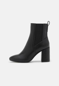 Schwarze Leder-Stiefeletten mit spitzem Zehenbereich, Blockabsatz und elastischen Seitenpaneelen. Glatte Textur mit einer Zuglasche hinten für einfaches Anziehen.