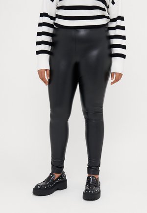 Black faux leather leggings with a glossy finish, featuring a slim fit and tapered ankles. Worn with a black and white striped sweater and chunky shoes.