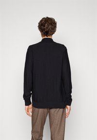 Svart stickad cardigan med ribbad krage, långa ärmar och avslappnad passform. Utsmyckad med design på fållen och ärmsluten. Minimalistisk stil.