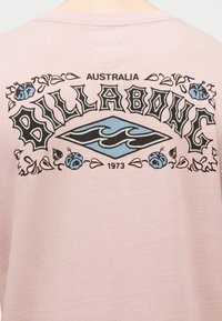 Billabongi logo ja tekst helel roosas kangas, millel on mustad ja sinised lained, lilleselemendid, detailid "Australia" ja "1973".