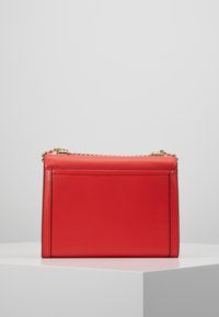 Rød læder crossbody taske med en struktureret rektangulær form, guldfarvet hardware og en kædetraspen, der har en glat tekstur.