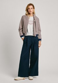 Rutet bomberjakke med marineblå ribkant, grå sweatshirt med tekst, højtaljede navy bukser med vidde og hvide stilfulde sneakers.