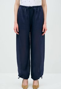 Navyblauwe wijde broek van lichtgewicht stof, met een trekkoord in de taille en verstelbare manchetten, gecombineerd met beige puntige hakken.