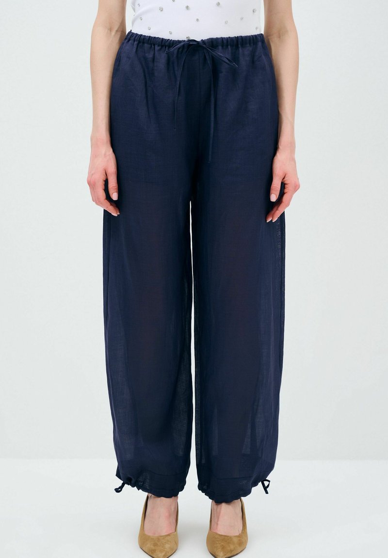 Navyblauwe wijde broek van lichtgewicht stof, met een trekkoord in de taille en verstelbare manchetten, gecombineerd met beige puntige hakken.