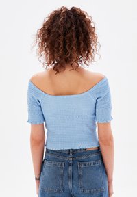 Světlomodrý crop top bez ramínek s krátkými rukávy, s nařasenou texturou a třepícím se lemem, kombinovaný s džíny s vysokým pasem.