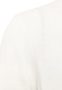 Pull en maille blanc avec un détail de couture. La texture semble douce et lisse. Pas de motifs ou d'accents visibles. Gros plan sur la zone de l'épaule.