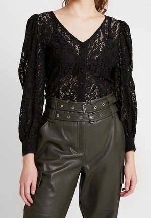 Zwarte kanten V-hals blouse met lange pofmouwen gecombineerd met hooggetailleerde olijfgroene leren broek met dubbele gespbanden.