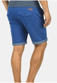 Pantaloni corti in cotone blu con orlo arrotolato, due tasche posteriori e un accento in pelle. Caratterizzati da un taglio dritto e una texture liscia.