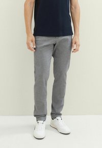 Grijze katoenen broek in een tapering fit, met zijzakken en elastische boorden, gecombineerd met witte sneakers op een neutrale achtergrond.
